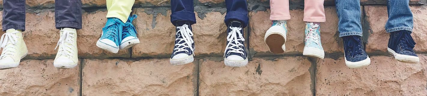 A row of children's sneakers and shoes lined up along a brick wall.